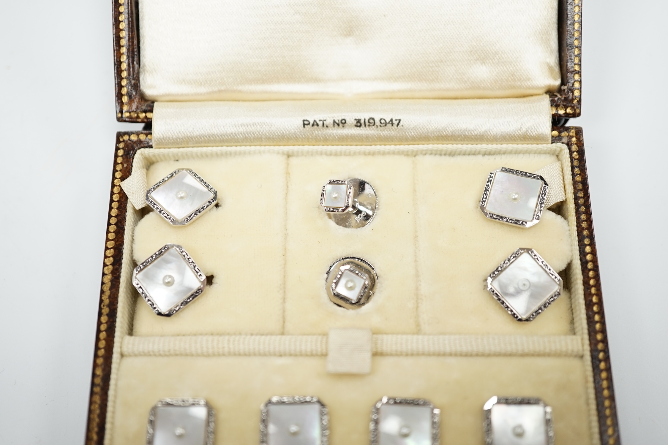 A 9ct white metal, mother of pearl and seed pearl set eight piece dress stud set, in fitted gilt tooled leather case.